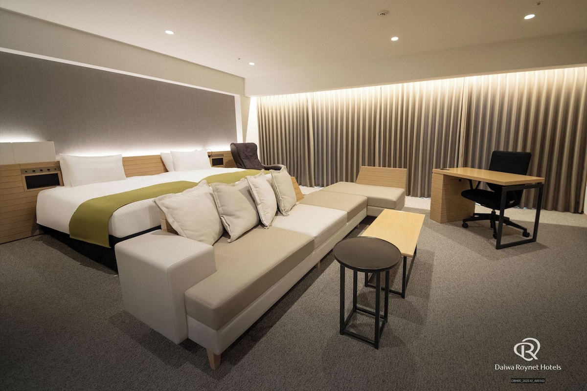 A modern hotel room with a large bed, a sofa, a desk, and a chair.