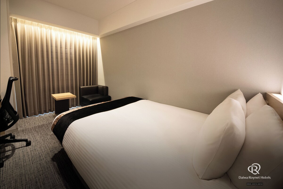 A hotel room with a large bed, a desk, a chair, and a curtain.