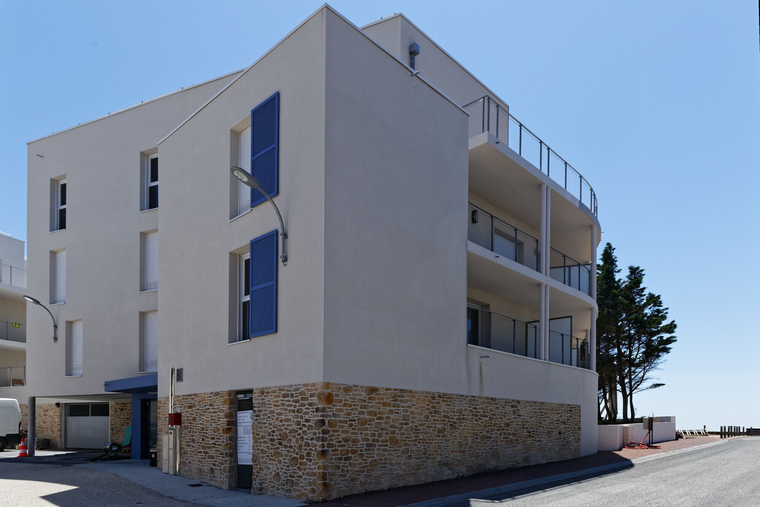 A modern multi-story building with a stone base, balconies, and a garage entrance.