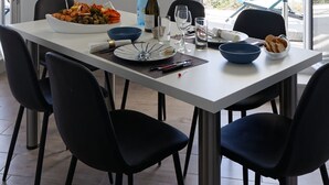 A dining area with a white table, black chairs, a painting, and a view through the glass door. - Facing the sea - 50 m from the  beach (La Guérinière)