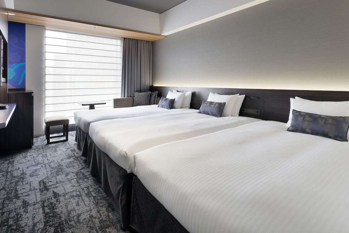 Una habitación de hotel con dos camas, un escritorio, una silla y un ventanal con persianas.