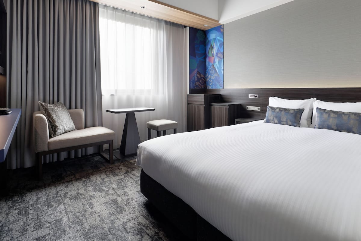 Habitación de hotel con cama, escritorio, silla, mesita y un cuadro en la pared.