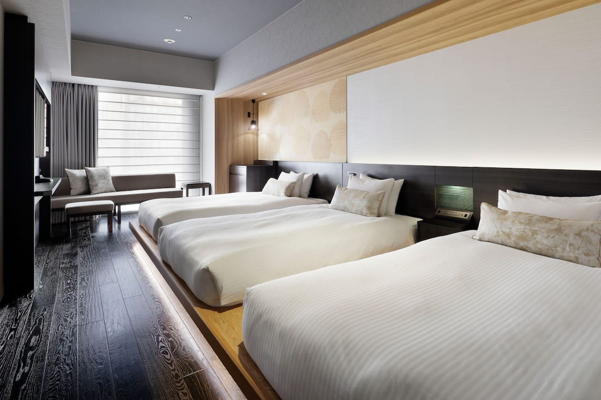Habitación de hotel con dos camas, un escritorio, una silla, un televisor y un ventanal con cortinas.