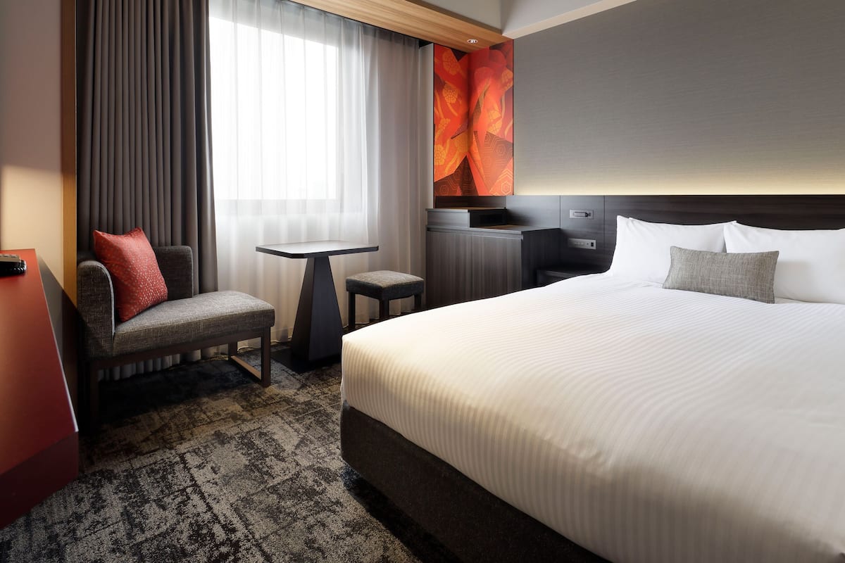 Una habitación de hotel con cama, escritorio, silla y ventana con cortinas.