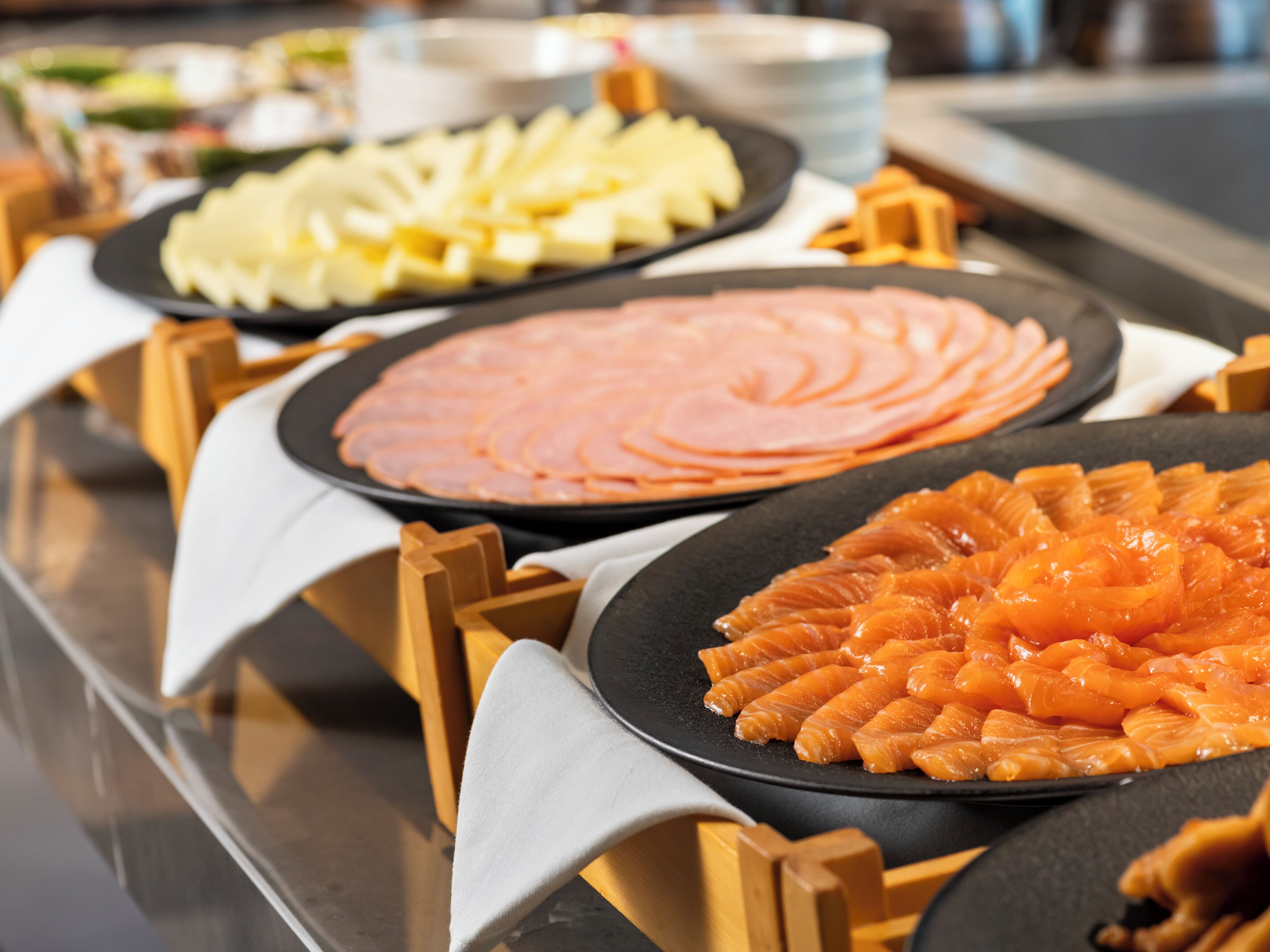 A buffet with various food items including sliced ham, cheese, and salmon arranged on black plates.