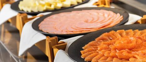 A buffet with various food items including sliced ham, cheese, and salmon arranged on black plates.
