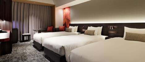 A hotel room with three beds, a desk, a chair, a small table, and a large window with curtains.