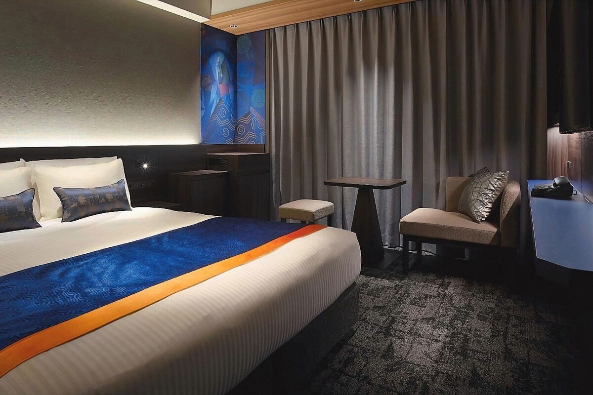 Una habitación de hotel con una cama grande, un escritorio, una silla y un cuadro en la pared.