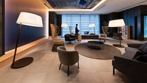 A modern hotel lobby with a large seating area, floor lamps, and a view of the city through large windows. - Mitsui Garden Hotel Ginza Gochome (Tokyo)