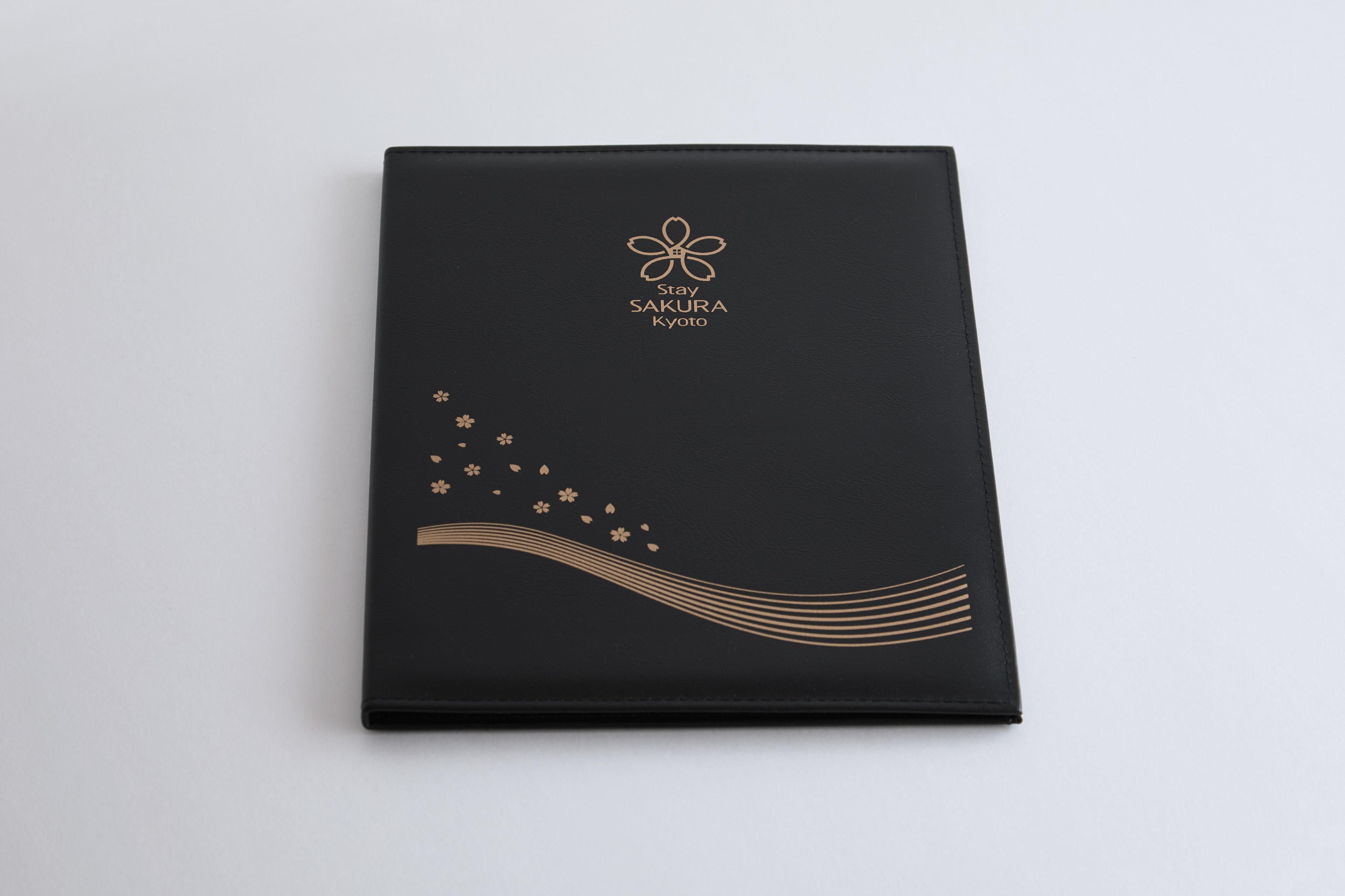 A black folder with gold floral and wave designs, and the text "Stay Sakura Kyoto".