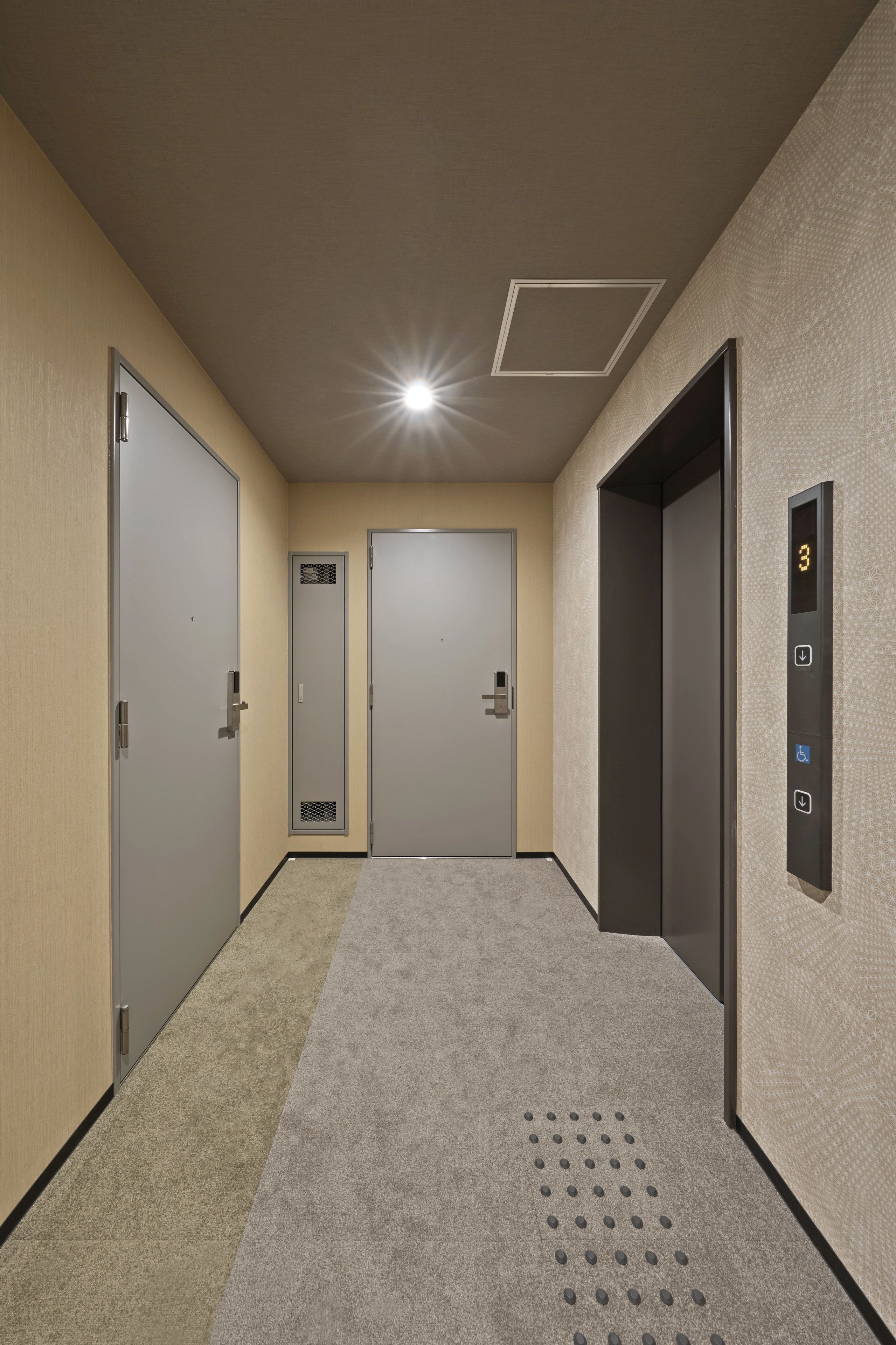 A hallway with three doors, a digital elevator control panel, and a patterned wall.