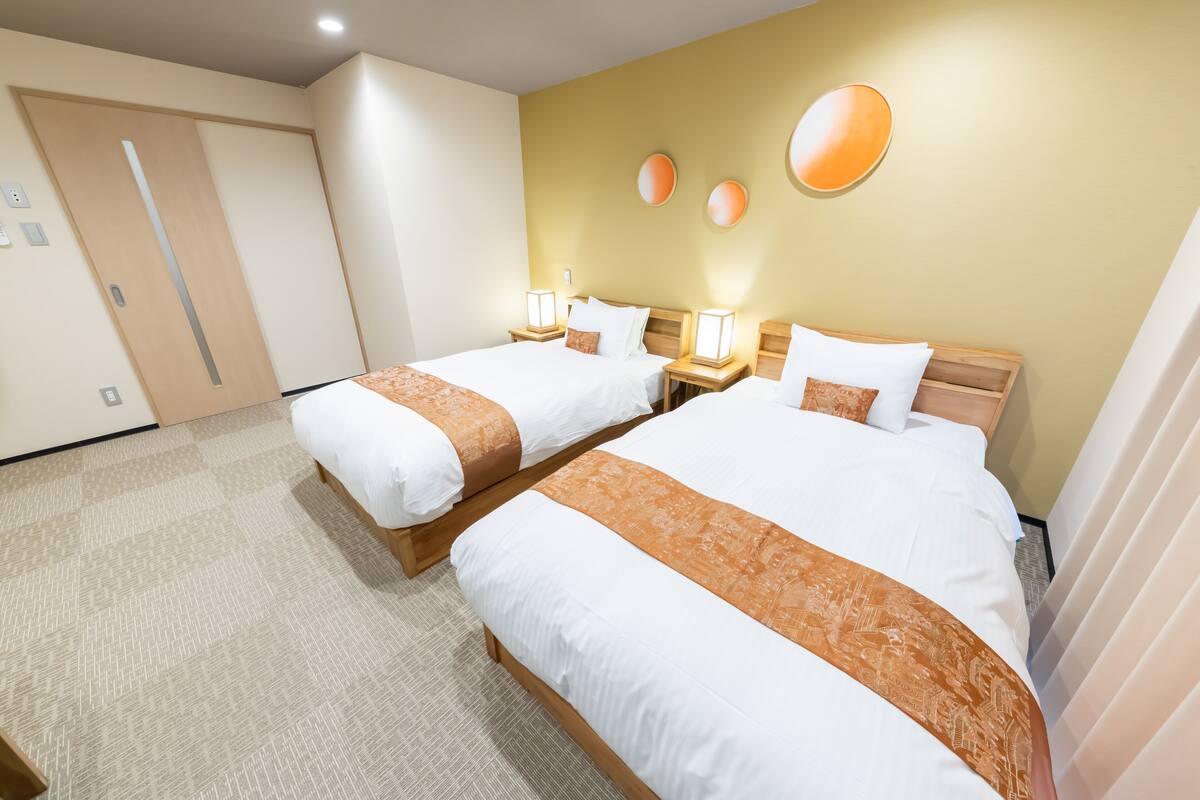 A hotel room with two beds, a wooden headboard, a beige carpet, and a wall with three circular light fixtures.