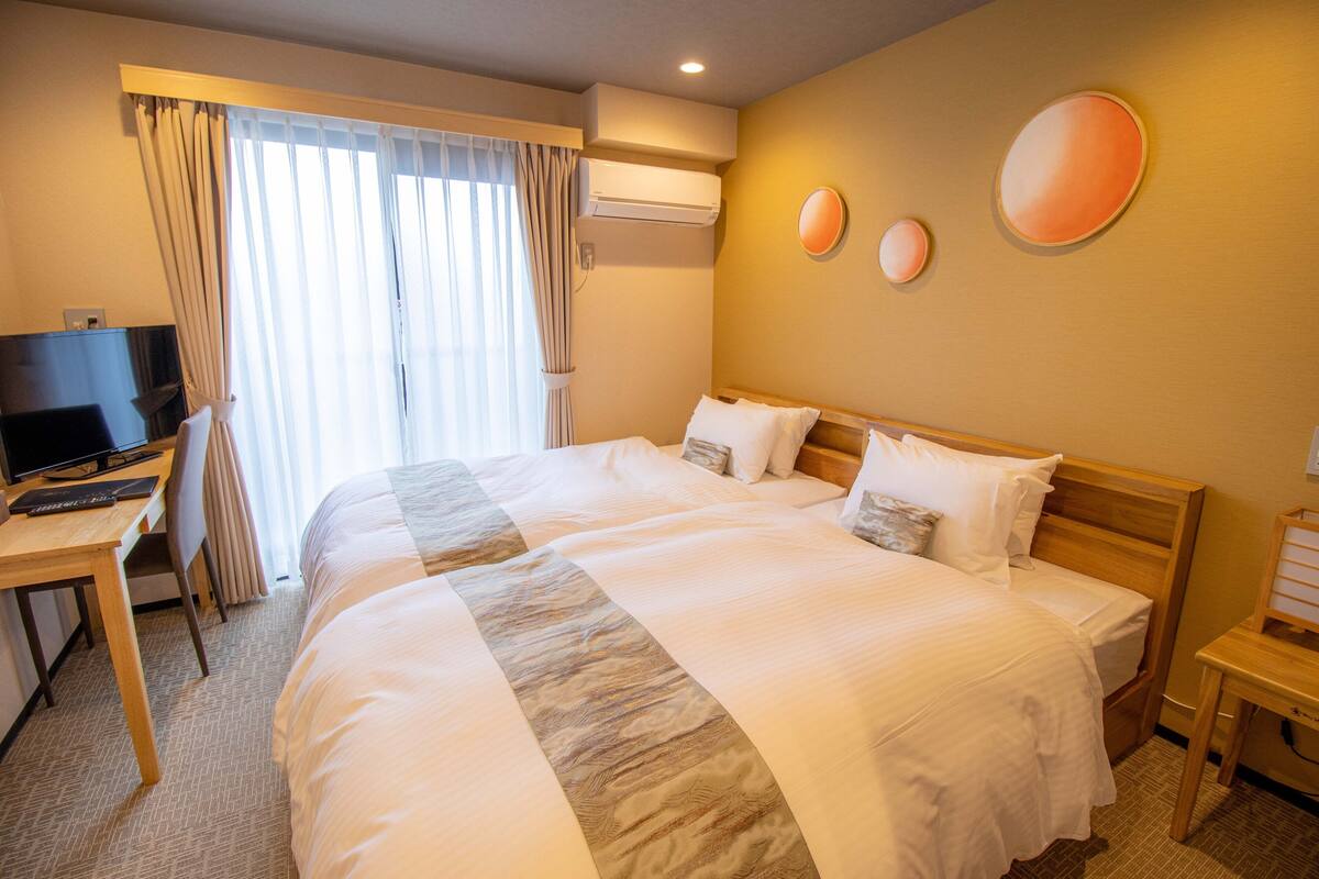 A hotel room with a large bed, a desk with a TV, and a window with curtains.