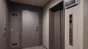 Un ascensor con una pantalla digital que muestra el número 1, un panel de control con botones y suelo alfombrado.