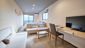 Una habitación de hotel moderna con sofá, una mesita, televisor y escritorio.
