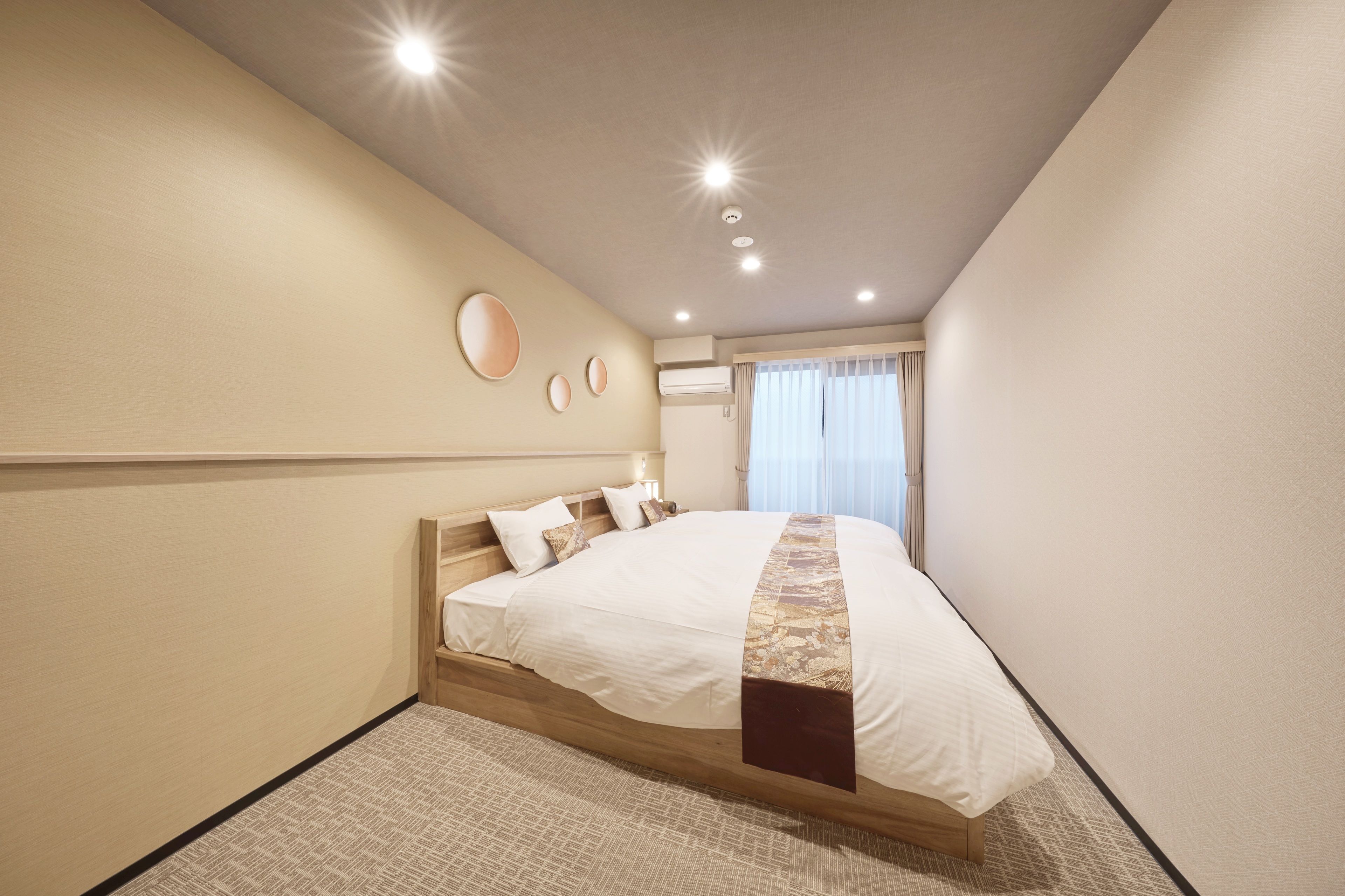 A hotel room with a large bed, a wooden headboard, a small bedside table, and a window with curtains.