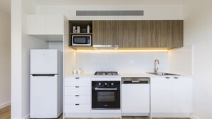 A modern kitchen with white cabinetry, a built-in microwave, a gas stove, and a dishwasher. - Q Squared Serviced Apartments (North Melbourne)