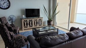 A living room with a sofa, a coffee table, a TV on a cabinet, a fan, and a plant. - Fantastic view!!!! Romantic setting (Rosarito Beach)