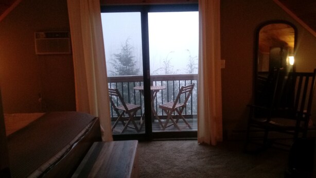 Ein Zimmer mit einer Schiebetür und einem Balkon, auf dem zwei Holzstühle stehen.