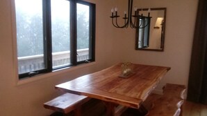 Ein Essbereich mit einem Holztisch und Bänken, einer Kandelaber und einem großen Fenster mit Blick auf Bäume.