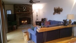 Ein Wohnzimmer mit Kamin aus Stein, einem blauen Sofa, einem Holztisch und einer Lampe.