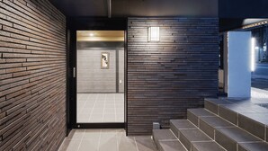 Una entrada de edificio moderno con un muro de ladrillo, una puerta de cristal y una escalera que sube.