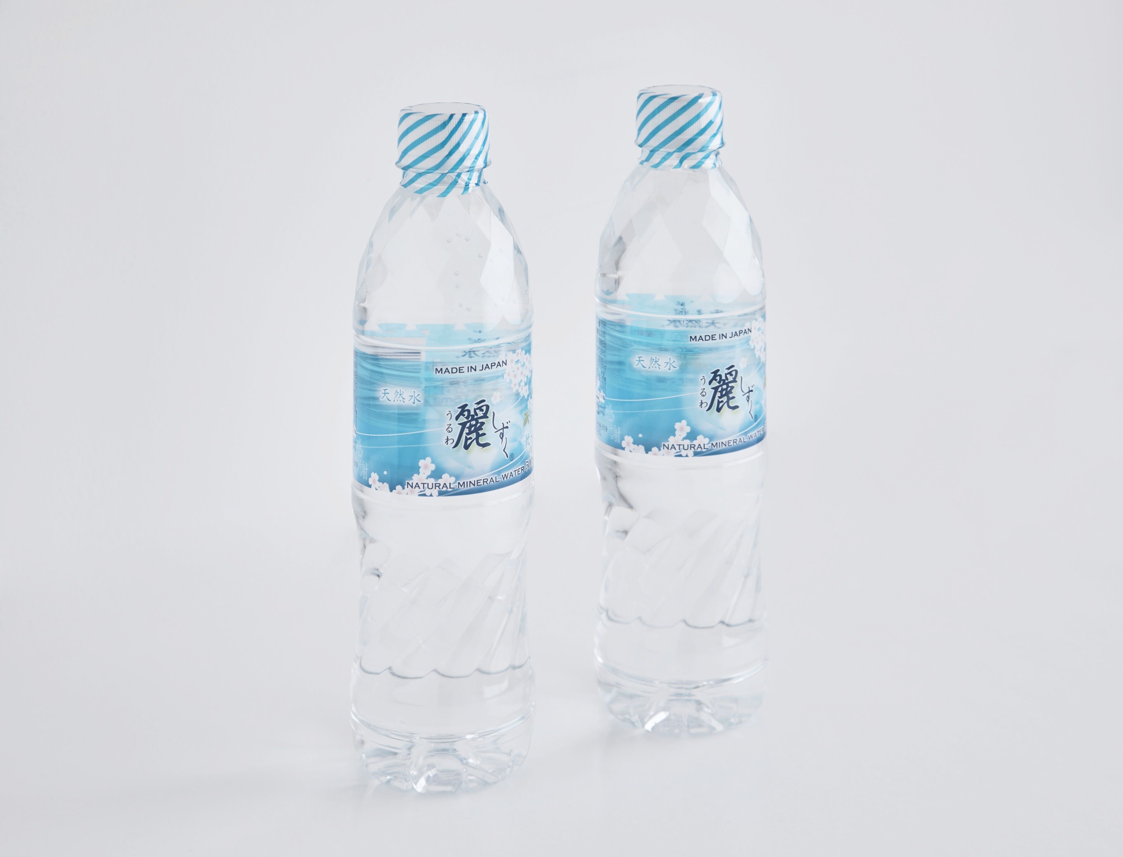 Two clear plastic water bottles with blue labels and striped caps, labeled "Made in Japan" and "Natural Mineral Water".