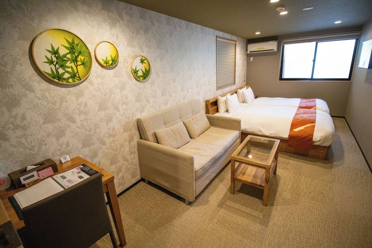 A hotel room with a bed, a sofa, a small table, and wall art.