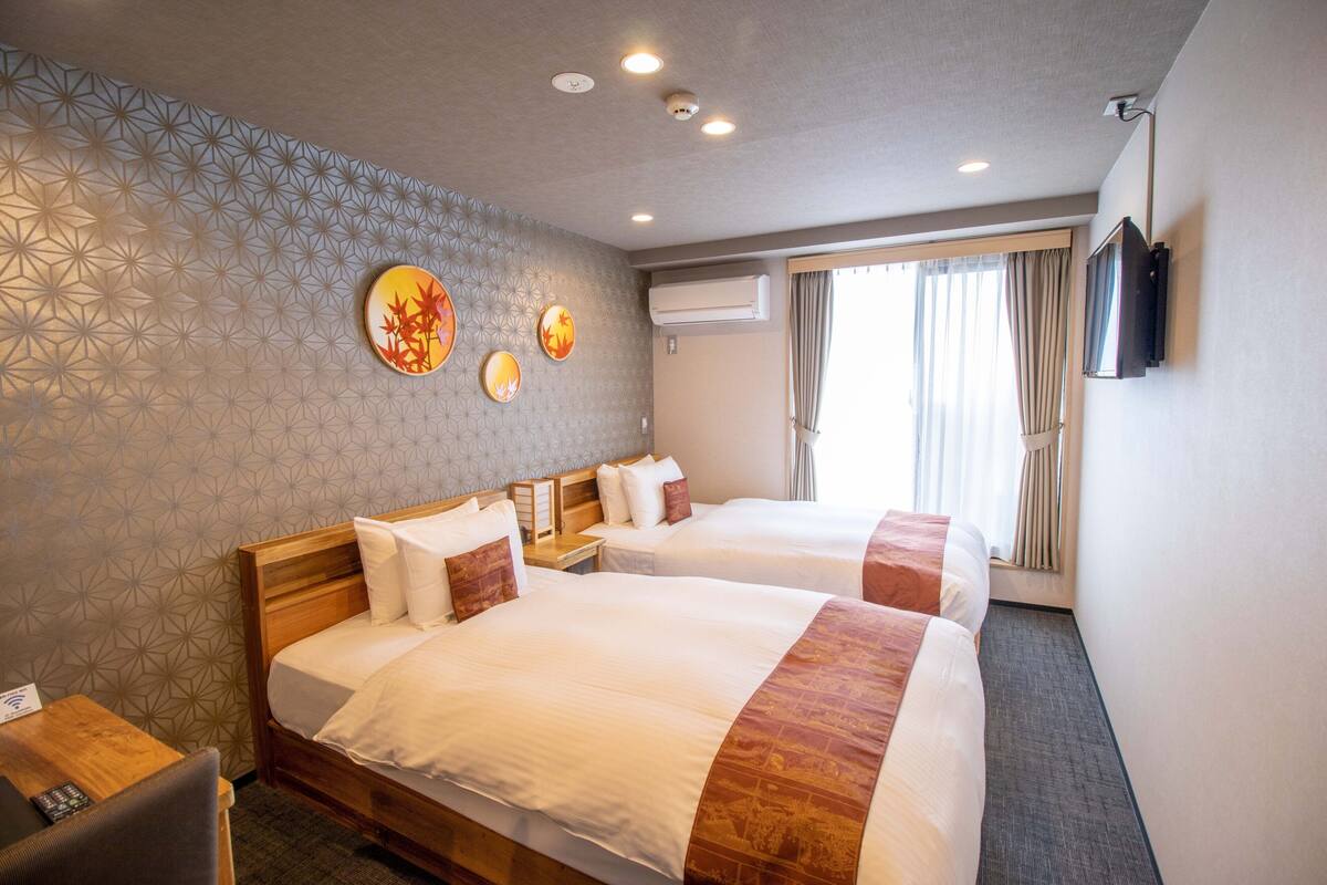 A hotel room with two beds, a wall-mounted TV, and a window with curtains.