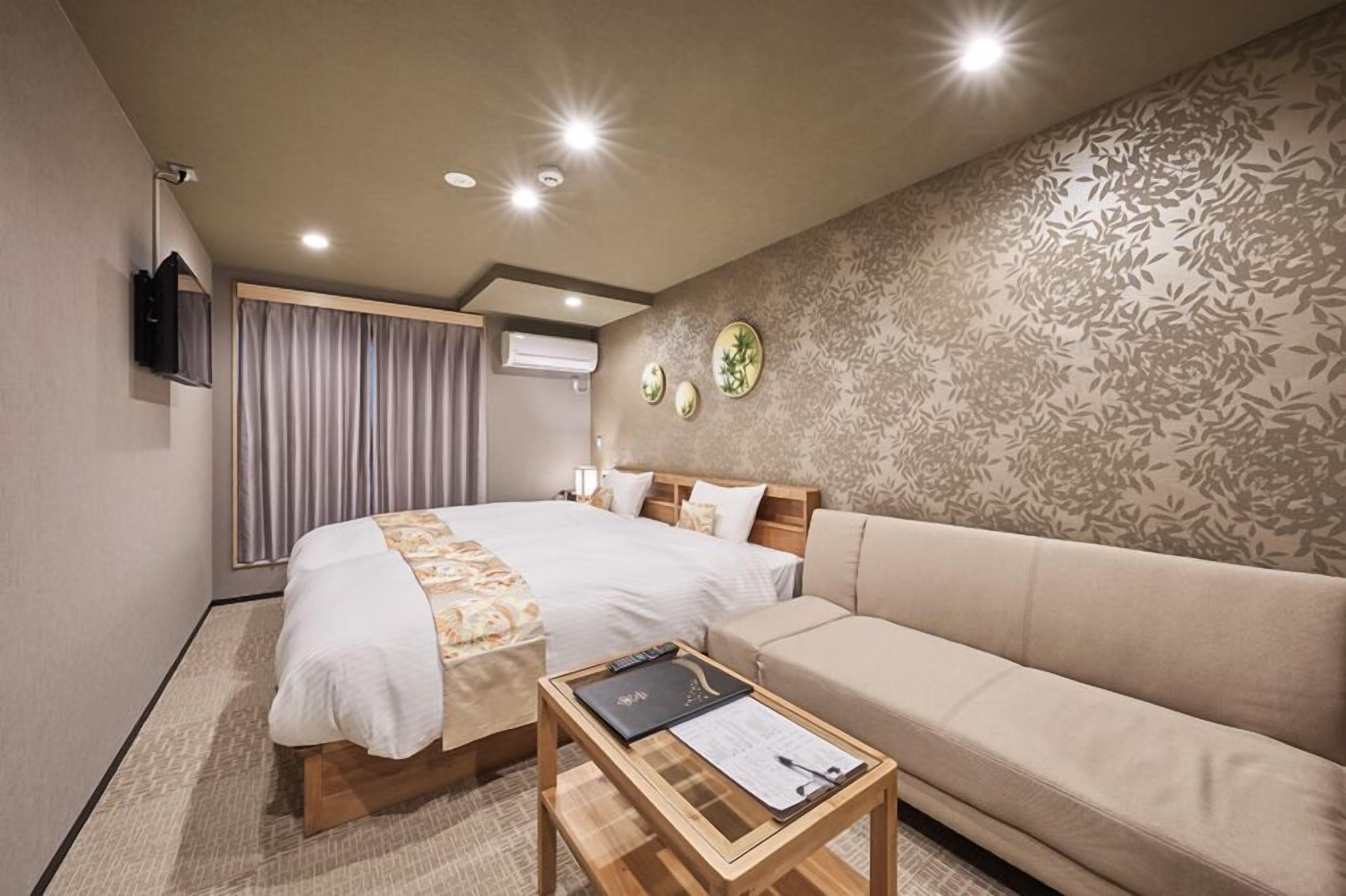 Een hotelkamer met een bed, een bank, een kleine tafel met een map en een aan de muur bevestigde televisie.