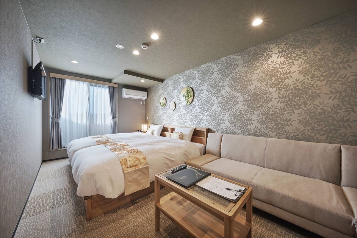 A hotel room with a large bed, a sofa, a small table, and a TV mounted on the wall.