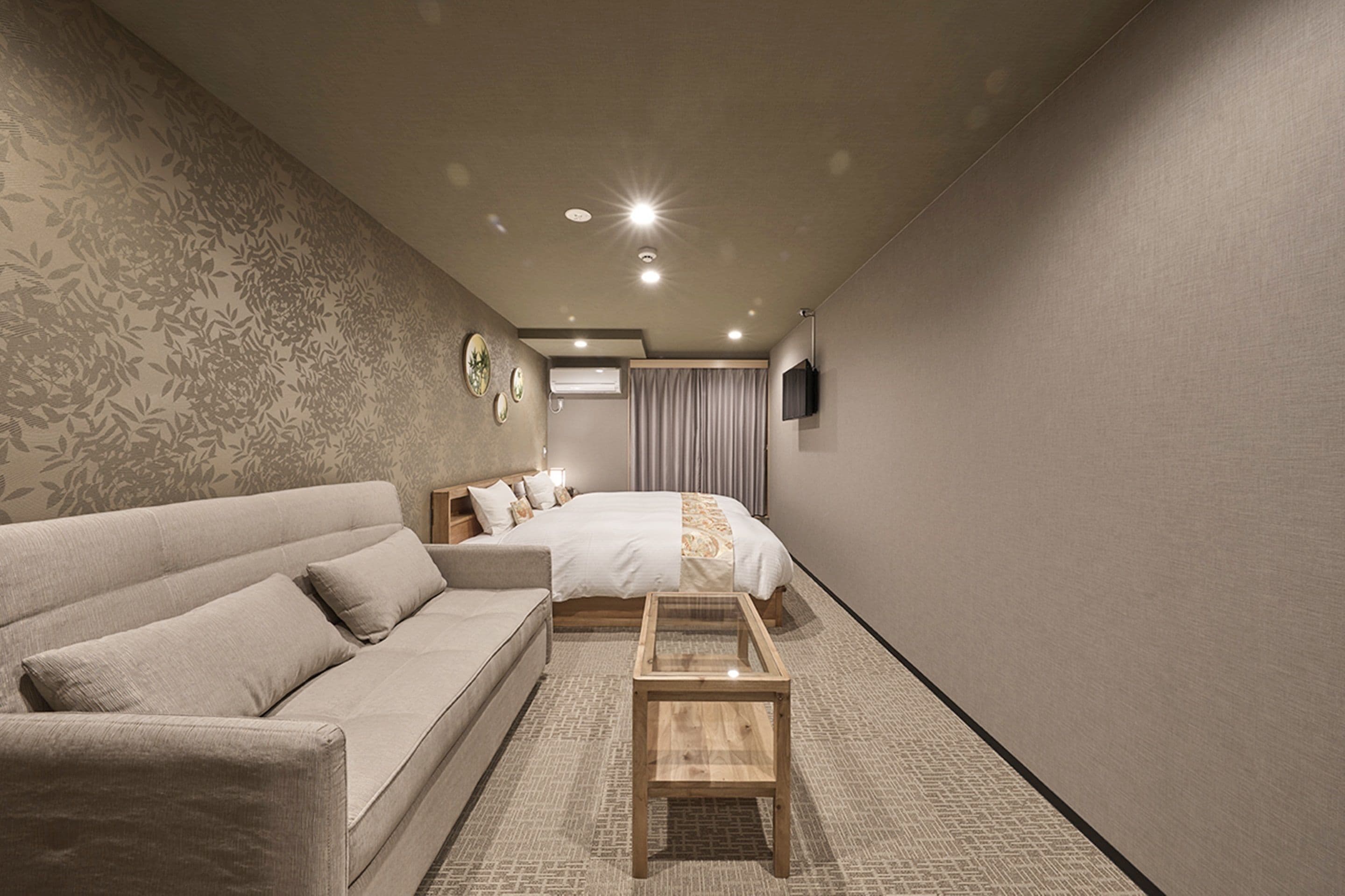 Ett modernt hotellrum med en soffa, en säng, ett soffbord i trä och en tv på väggen.