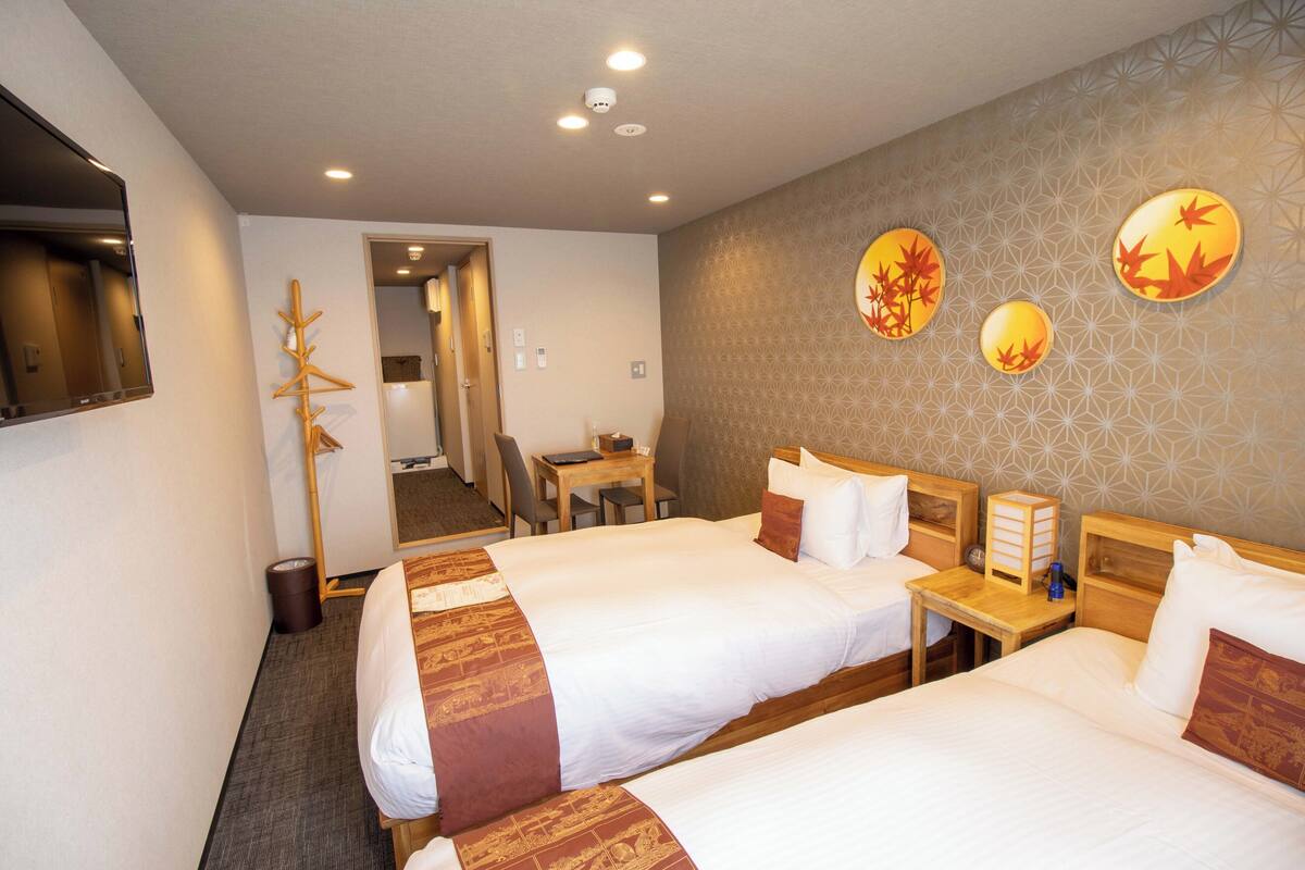 A hotel room with two beds, a desk, and a chair. There is a mirror on the wall and a door leading to a hallway.