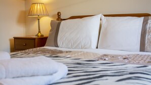 A neatly made bed with a zebra print blanket, a bedside lamp, and a wooden nightstand. - Apartment 4, Skye Holiday Apartments, Phoenix Flats (Portree)