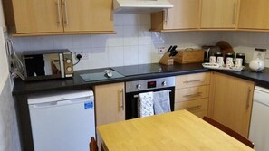 A compact kitchen with a microwave, toaster, and a small oven. There is a wooden table and a sink with a dish rack.