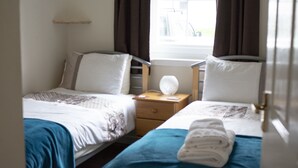 Een hotelkamer met twee bedden, een nachtkastje, een lamp en een raam met gordijnen.