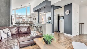 A modern kitchen with a central island, bar stools, and a dining area with a large window. - Compfortable Chalet to Rent at Stoneham located at the Mountain (CITQ: 287663) (Stoneham-et-Tewkesbury)