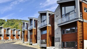 A row of modern multi-story buildings with balconies, numbered 22 to 26, featuring a combination of stone and wooden facades. - Compfortable Chalet to Rent at Stoneham located at the Mountain (CITQ: 287663) (Stoneham-et-Tewkesbury)