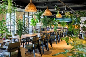 A modern dining area with multiple tables and chairs, surrounded by various indoor plants and hanging wicker lamps. - Maxx Jeju, A H WORLD Hotel (Jeju City)