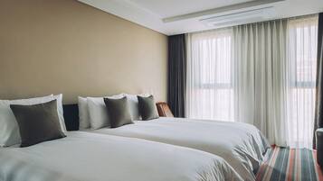 A hotel room with two beds, a chair, a desk, and a large window with curtains.