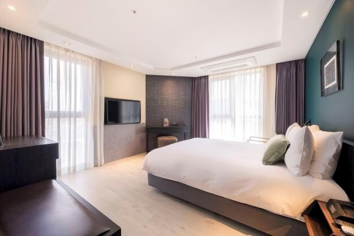 A modern hotel room with a large bed, a flat-screen TV, a fireplace, and a desk.