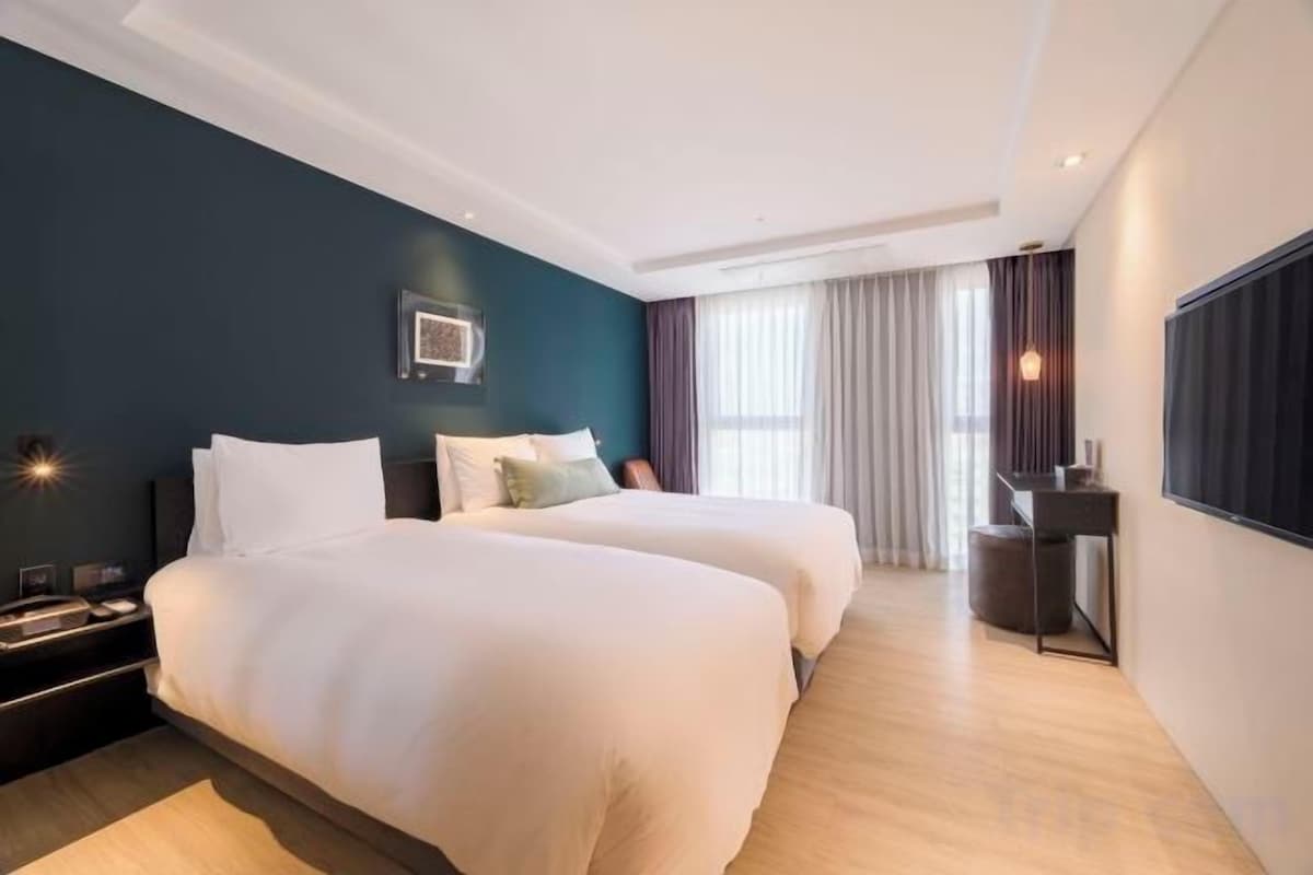 A hotel room with two beds, a desk, a chair, and a large window with curtains.