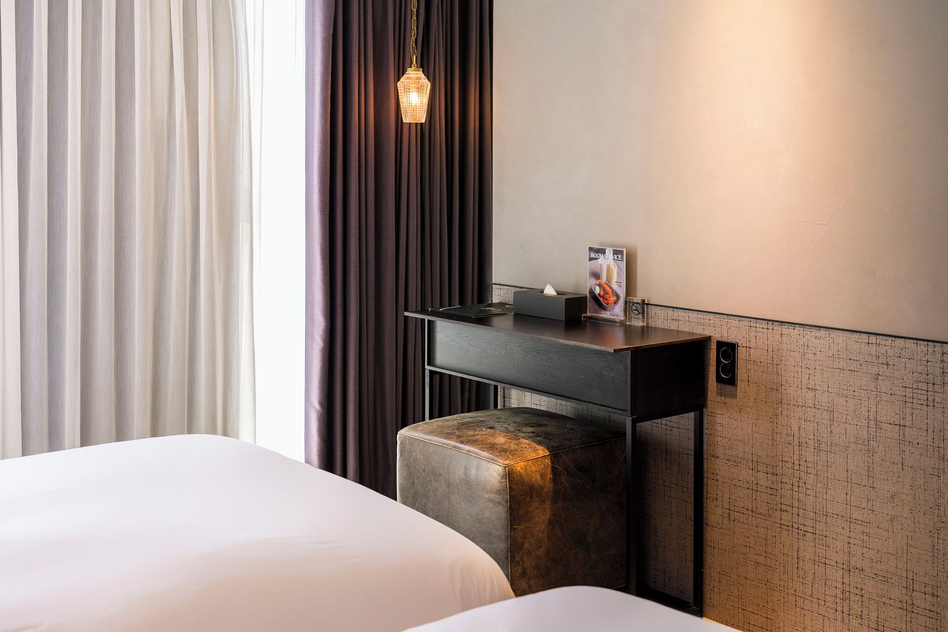 A hotel room with a bed, a bedside table with a tissue box, and a wall-mounted light fixture.