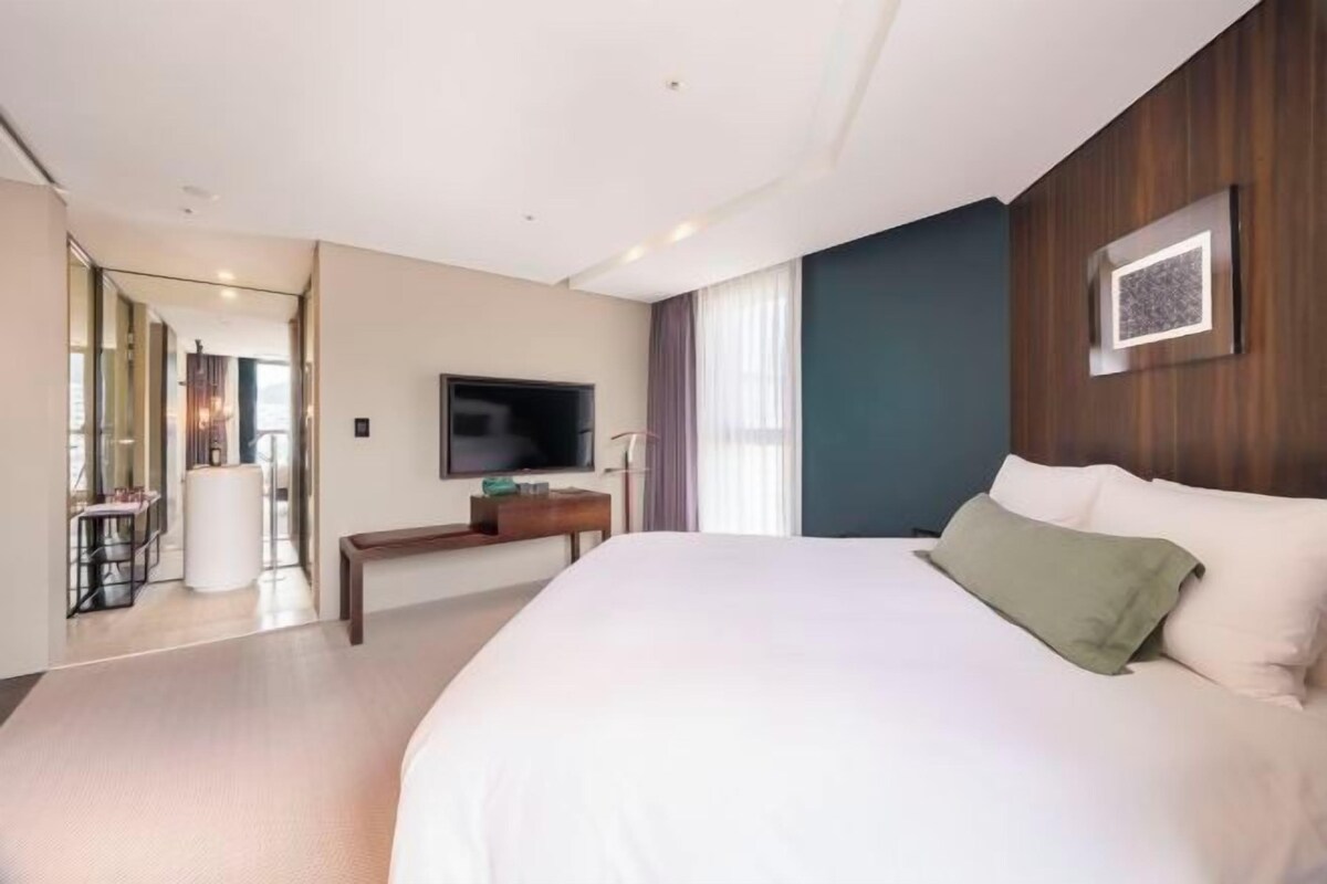 Une chambre d’hôtel dotée d’un grand lit, d’un téléviseur à écran plat, d’une tête de lit en bois et offrant une vue sur l’extérieur.