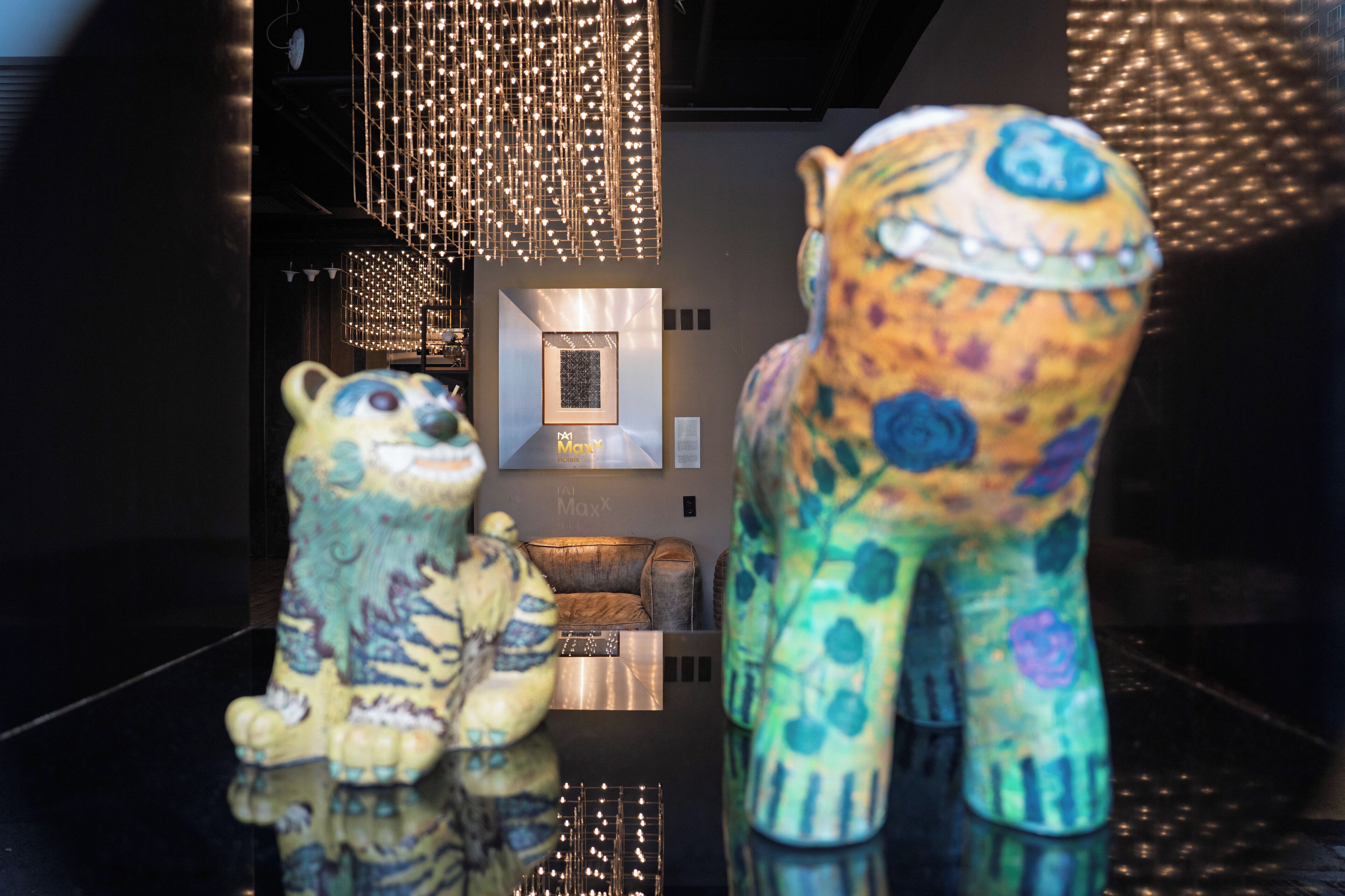 A modern interior with two colorful ceramic sculptures, a reflective floor, and a geometric light fixture.