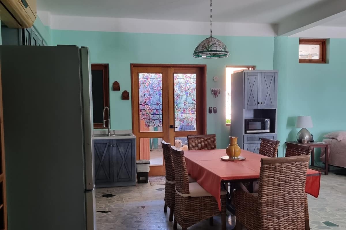 A spacious kitchen with a refrigerator, dining table, and wicker chairs.