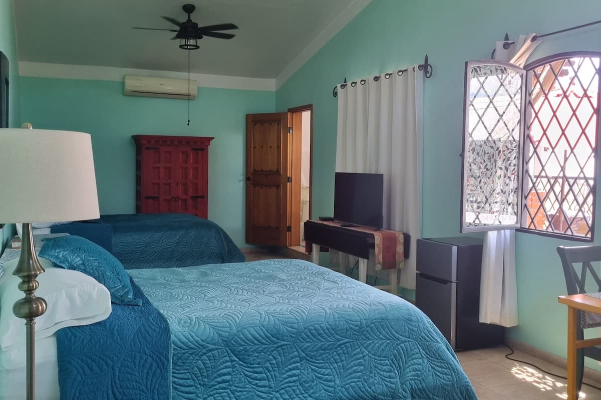A bedroom with a bed, a desk, a chair, a ceiling fan, and a window with curtains.