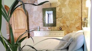 Ein Schlafzimmer mit Steinwand, Holztür, einem Bett mit Kissen, einem Nachttisch und einem Deckenventilator.