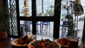 Ein Restaurant mit Terrassensitzgelegenheiten, Blick auf Palmen und einem Tisch mit Speisen und einem Getränk.