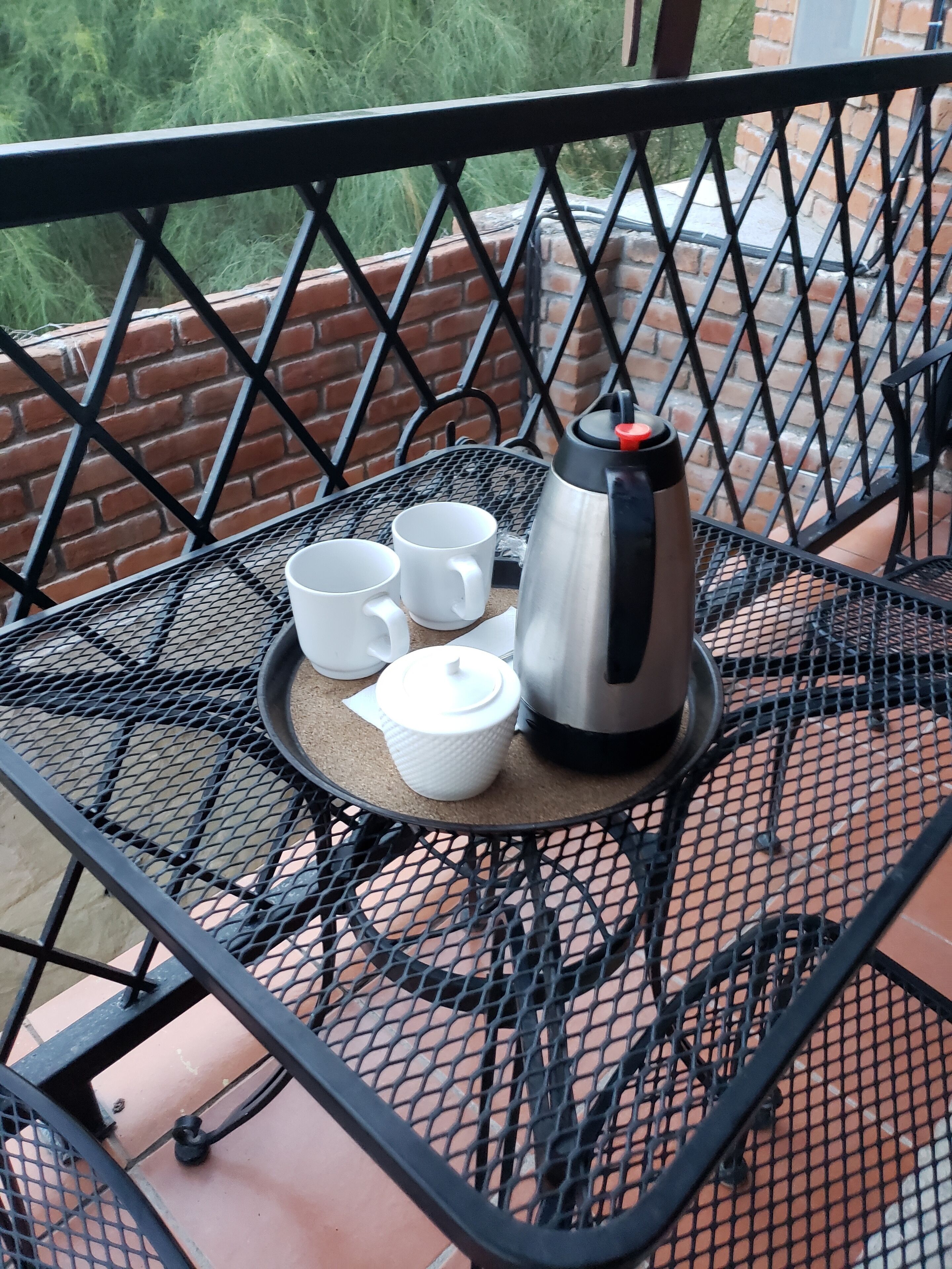A metal table with a tray containing a coffee pot, two cups, and a tissue box.